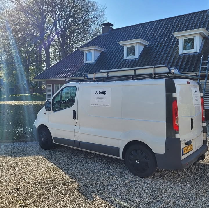 De witte bus van J. Seip met ladders op het imperiaal, voor een woning met dakkapellen