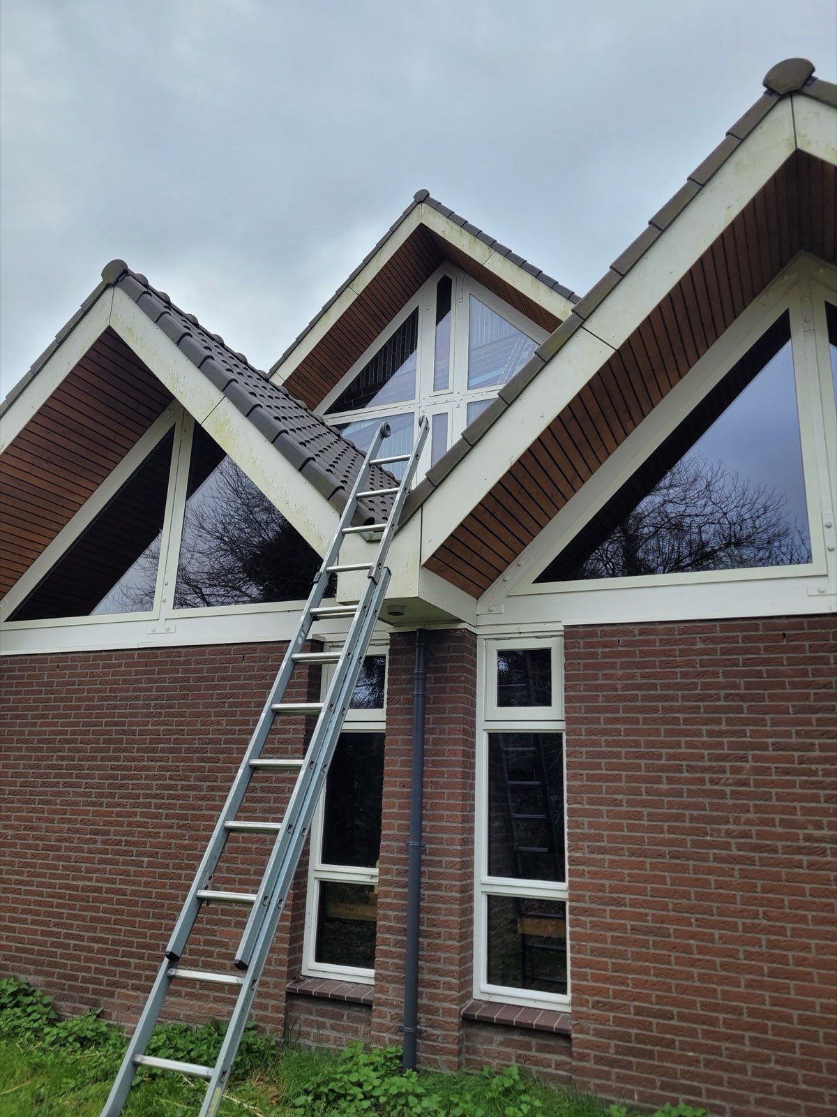 Ladder tegen een woning met grote driehoekige ramen in de puntgevels, tijdens het glazenwassen