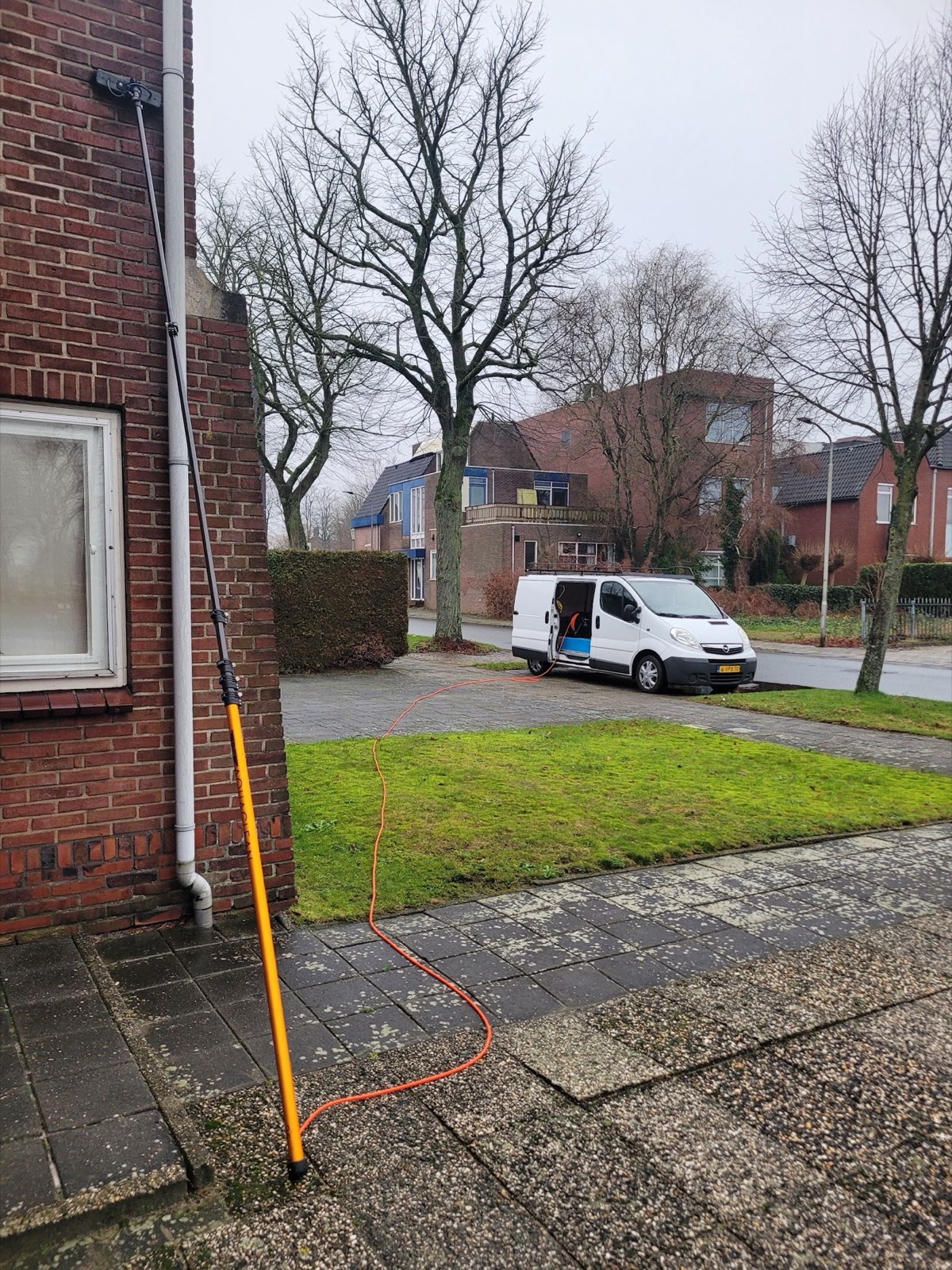 Telescoopsteel met waterslang tegen een bakstenen woning, de bus van J. Seip op de achtergrond
