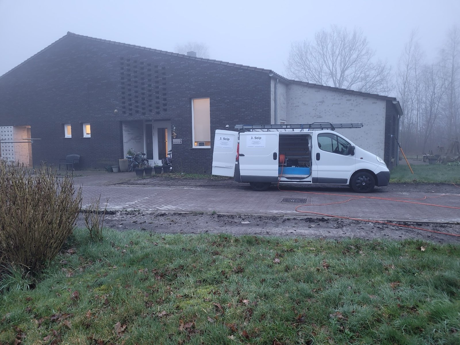 De bus met open deuren bij een donker bakstenen pand op een mistige ochtend