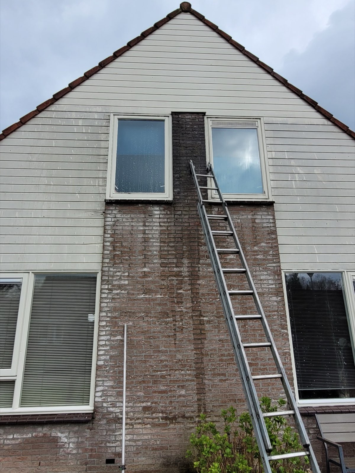 Ladder tegen een puntgevel met witte houten gevelbekleding en twee ramen